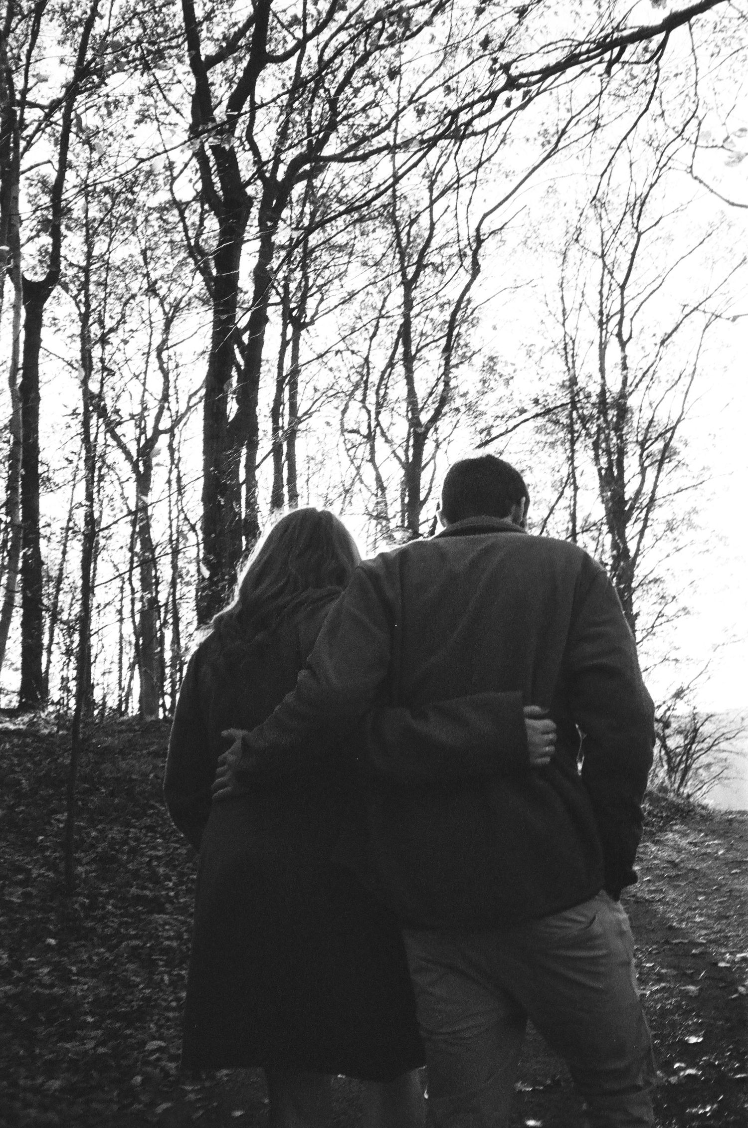 Black and white photo of a couple walking arm in arm through a bare winter forest.