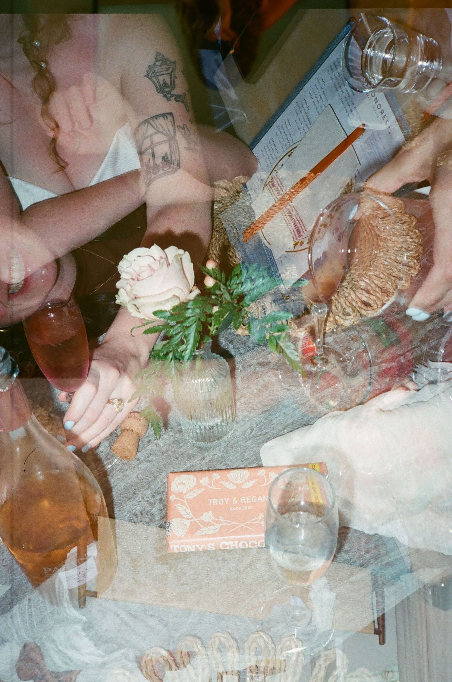 Double exposure film photo of wedding reception table with flowers, wine bottles, and decorative items.