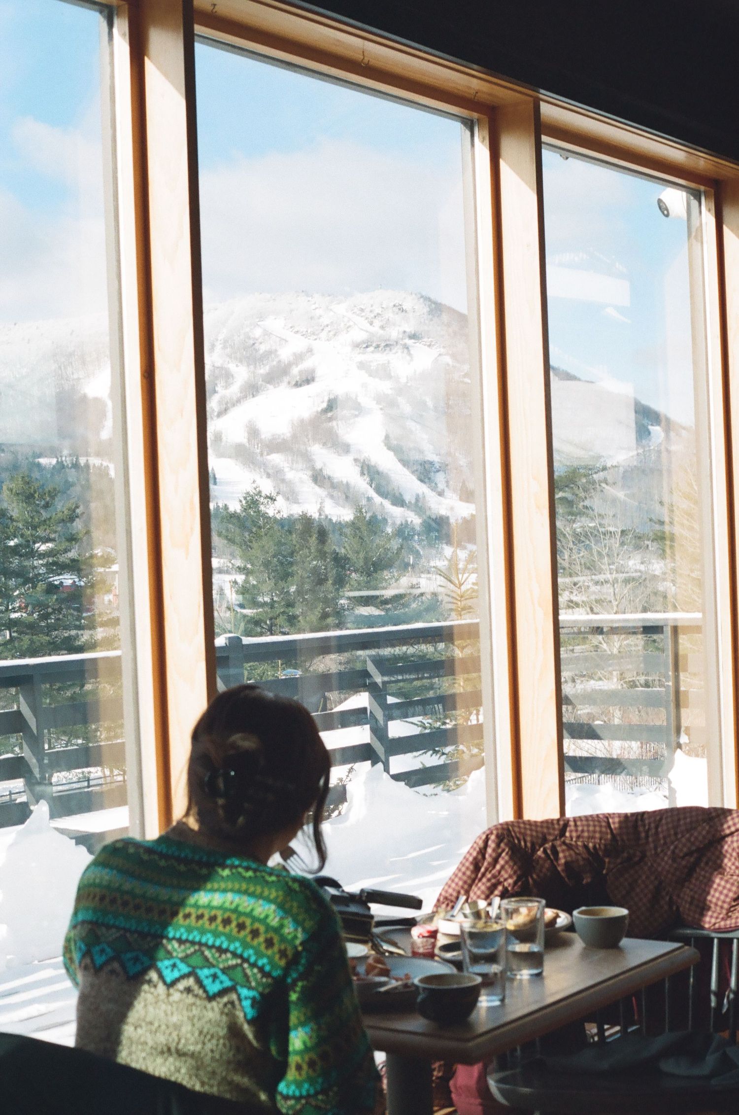 Two people dining indoors with a stunning snow-covered mountain view through large wooden-framed windows.