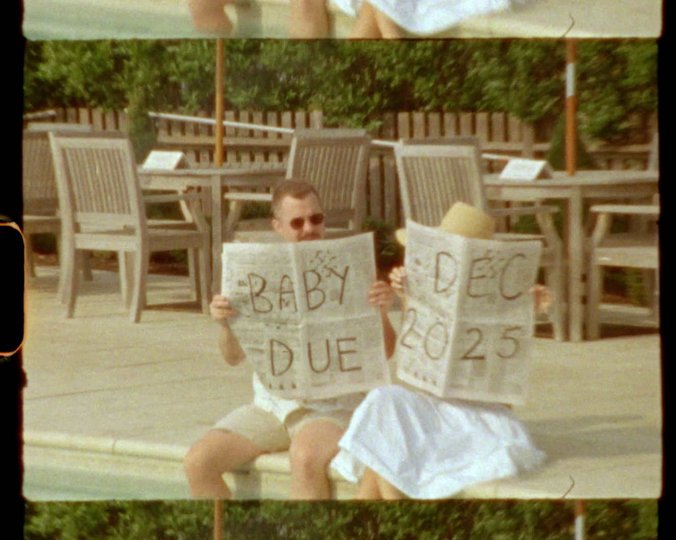 Couple sitting outdoors holding signs announcing Baby Due Dec 2025 in a charming pregnancy reveal photo.