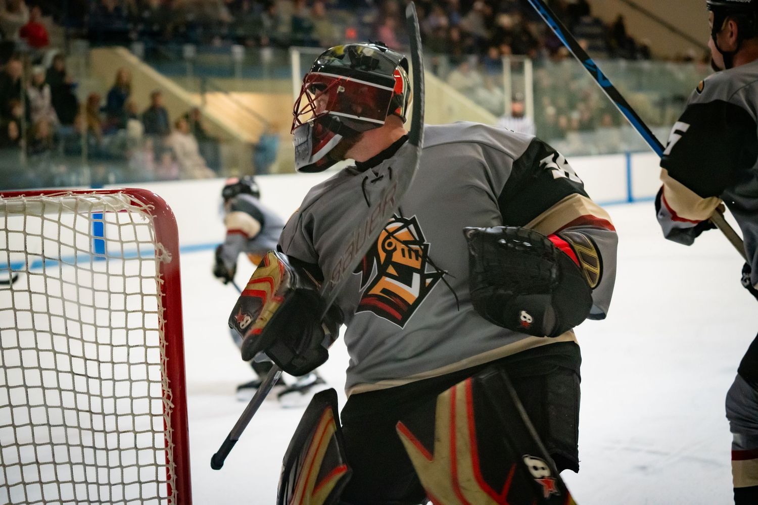 Hockey goalie in gray jersey and protective gear defends the net during game.