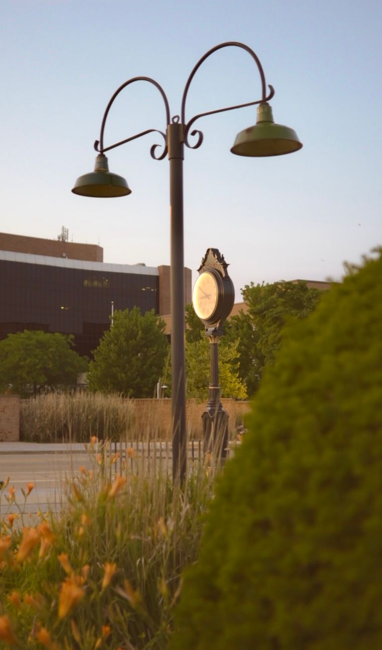 Decorative vintage street lamp with dual lights at dusk against urban landscape.