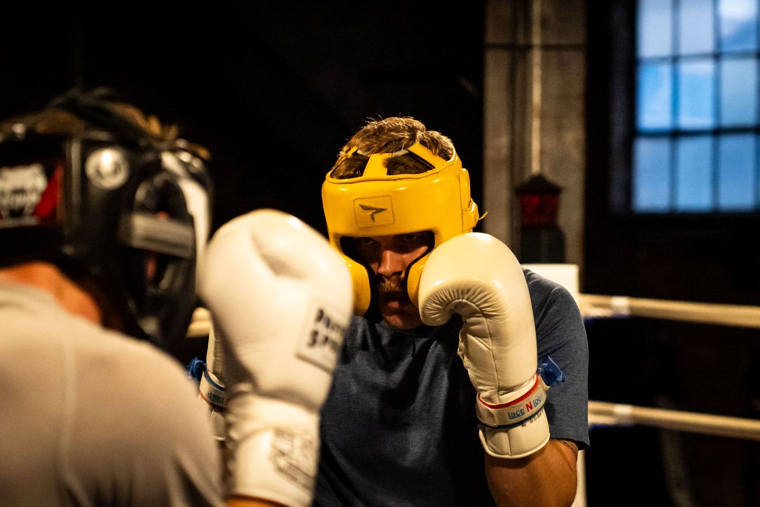 Boxing match in progress with fighters wearing protective gear near ring corner.