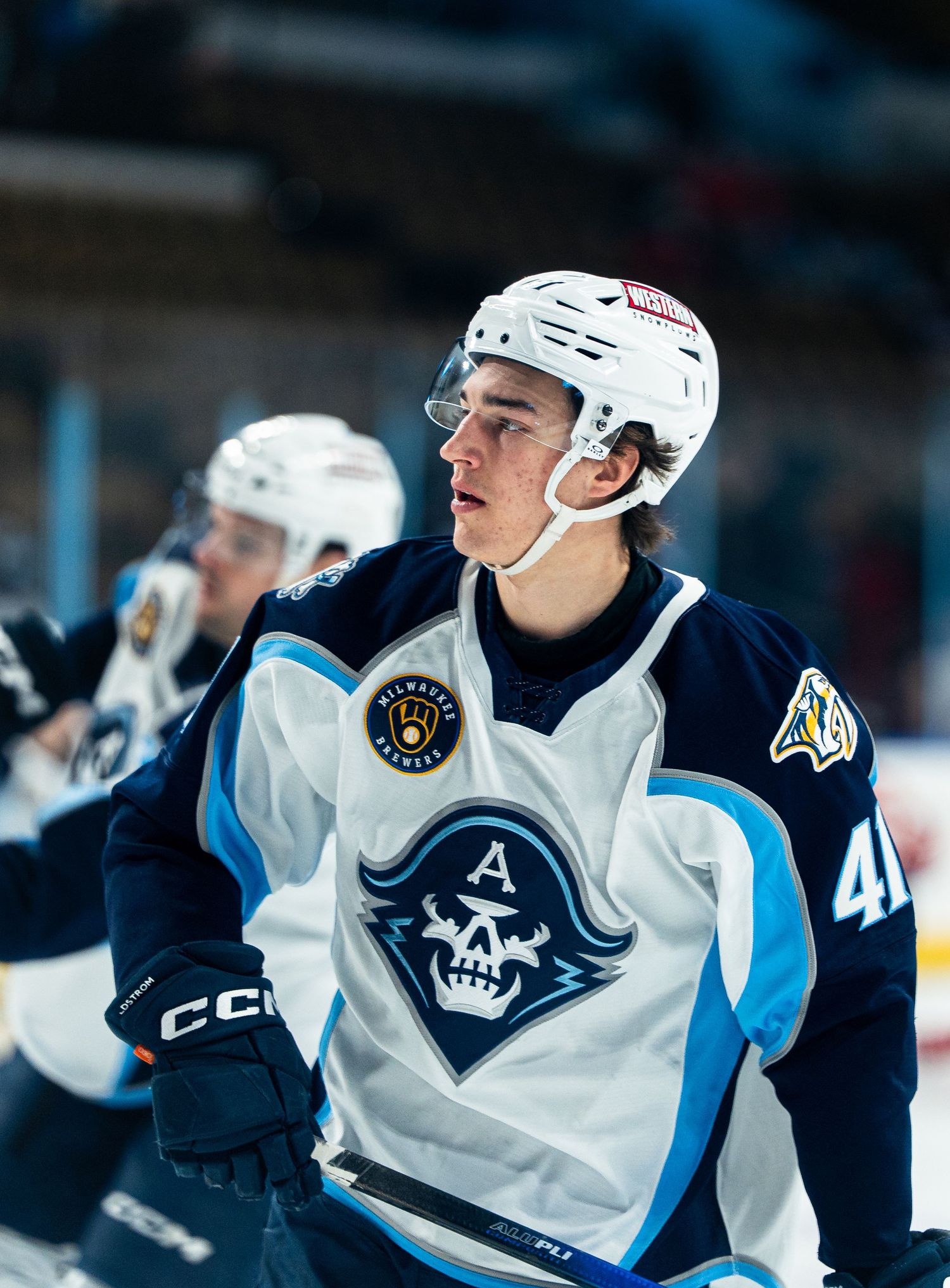 Professional hockey player in white and navy uniform with skull logo during game.