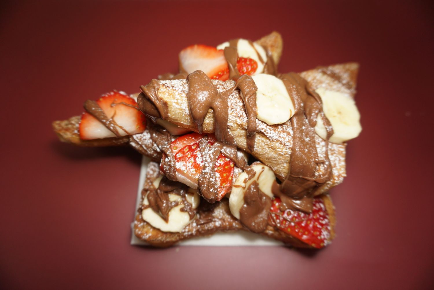 French toast with fresh strawberries and cream arranged on a red background.