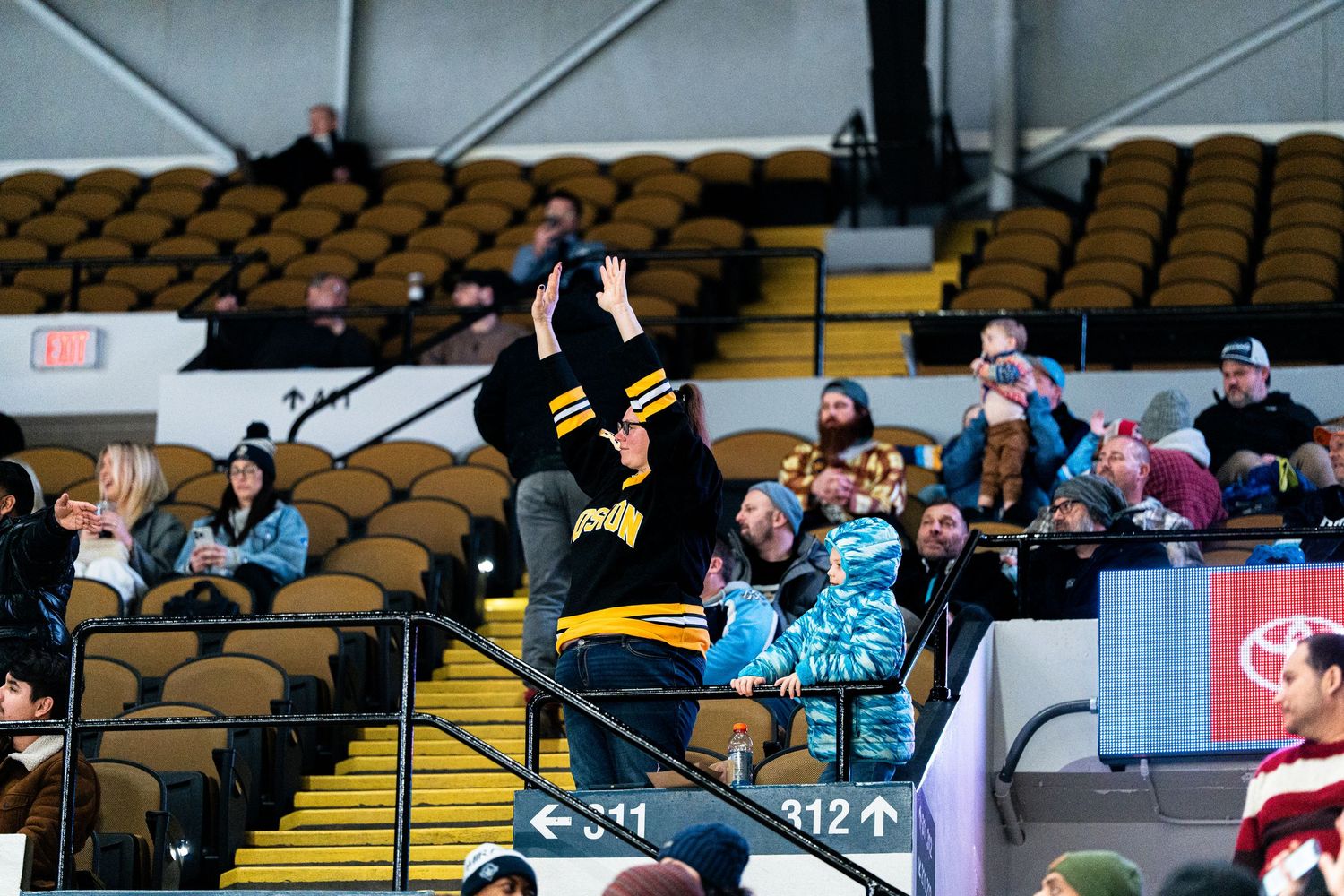 Scattered spectators watch from yellow seats in a hockey arena.