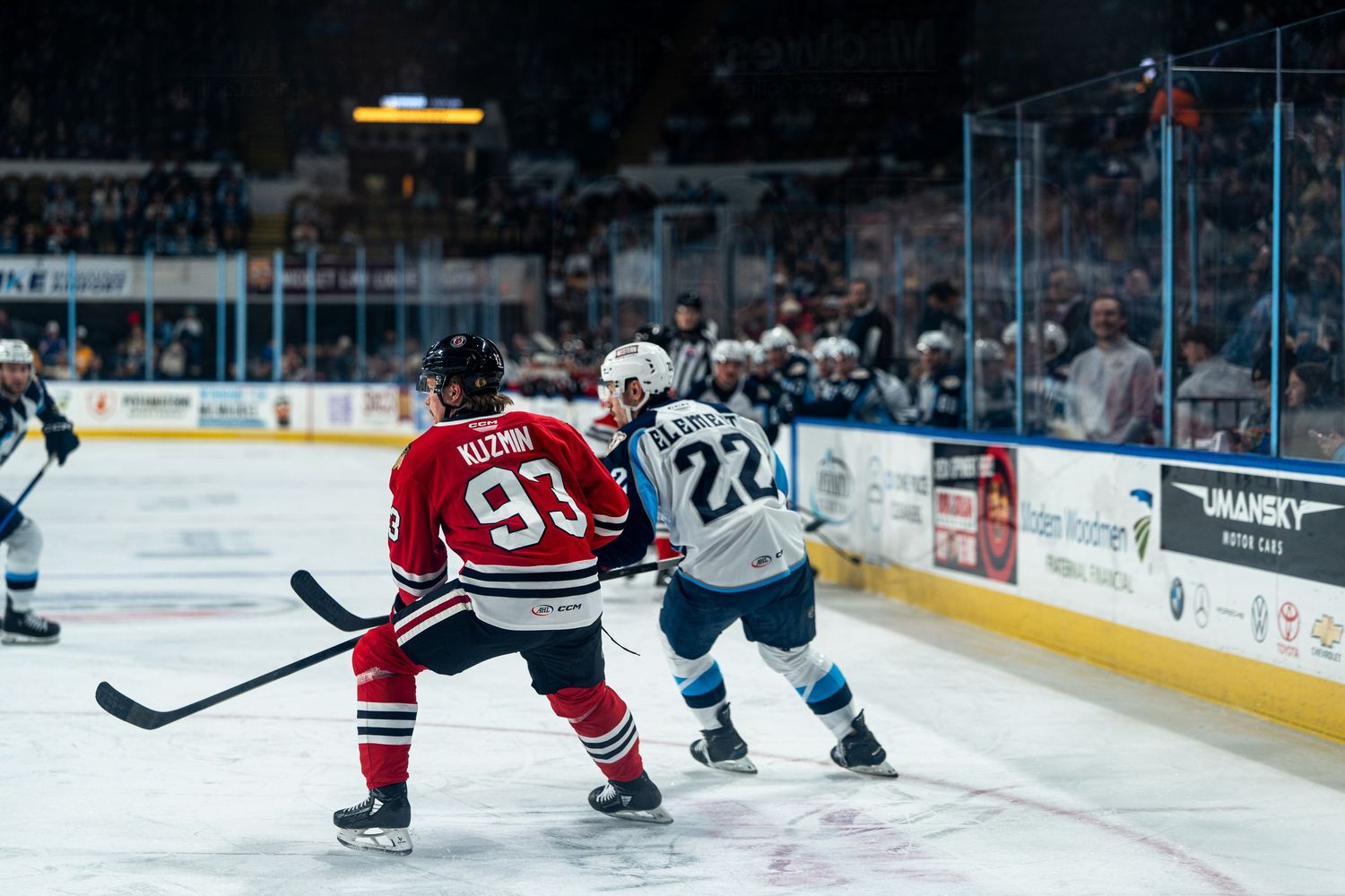 Hockey players in red and blue jerseys battling for puck position during game.
