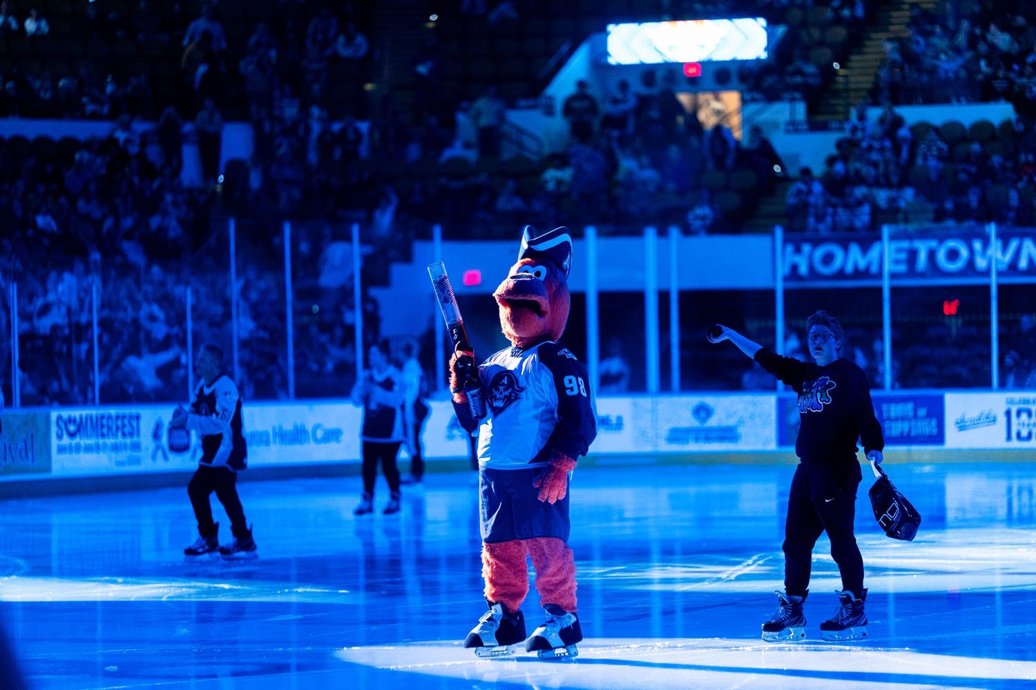 Young hockey fan in blue jersey waves to crowd during on-ice event.