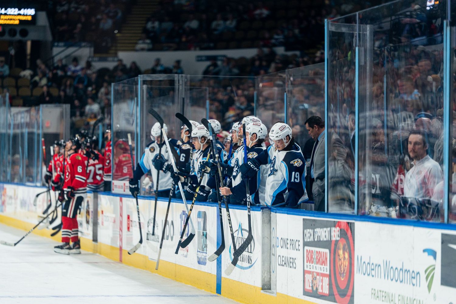Hockey players compete for the puck during an intense ice hockey match with spectators watching from the stands.