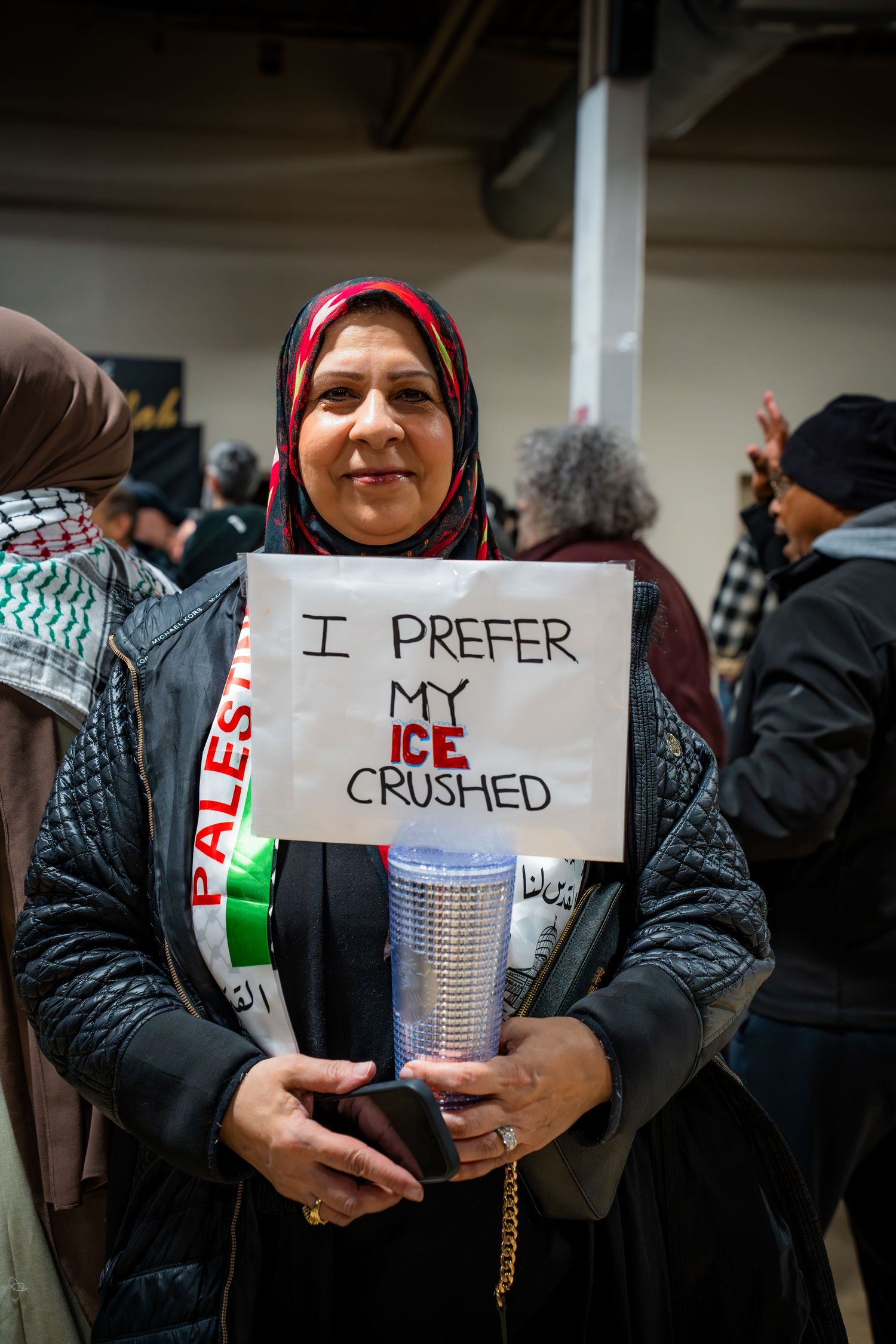 Woman in hijab holds sign reading I Prefer My ICE Crushed at protest rally.