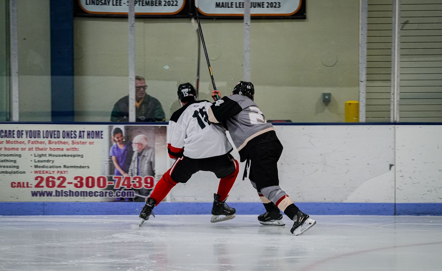 Two hockey players battle for position along the boards during intense game action.