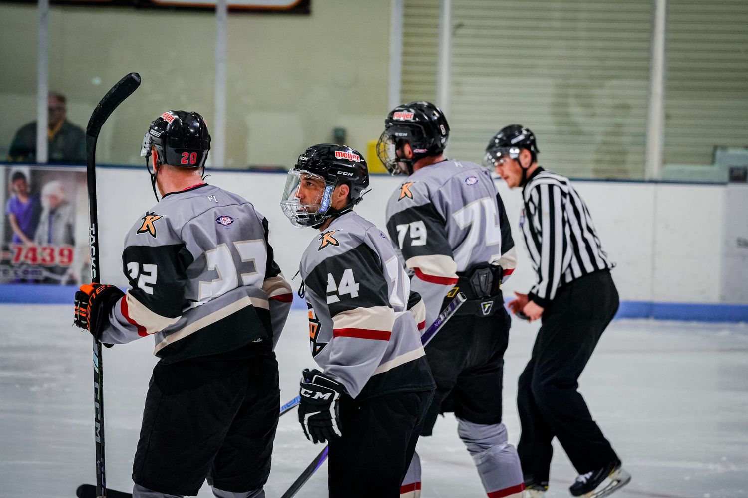 Hockey players and referee gather on ice during game stoppage.