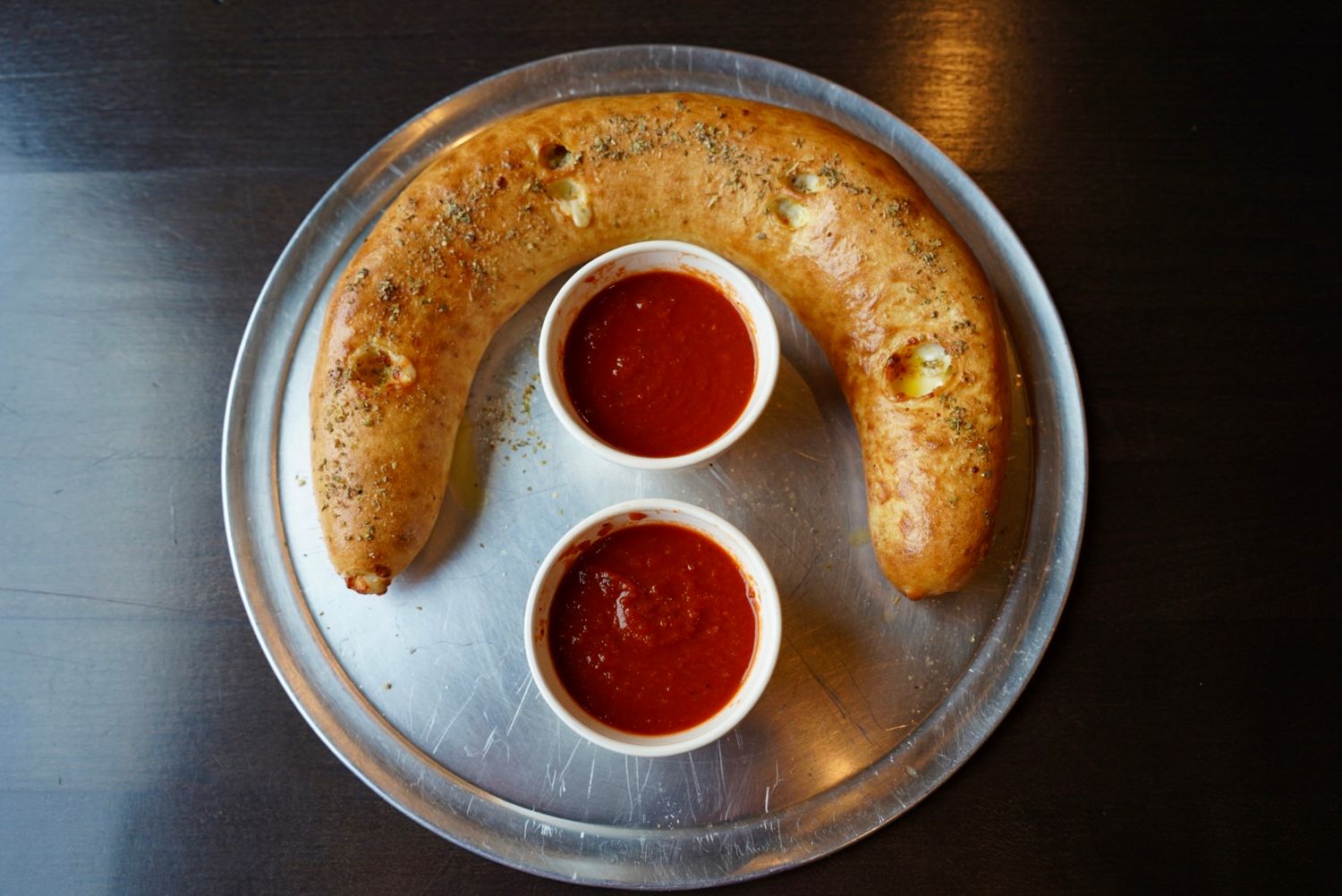 Calzone with red dipping sauce served on a silver platter.