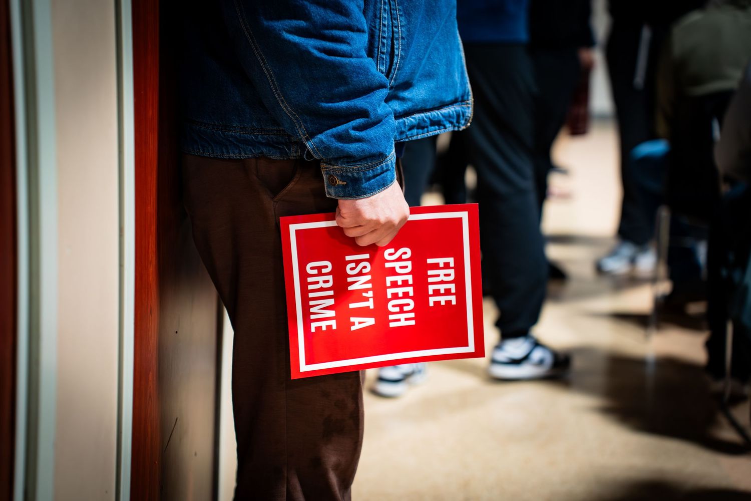 Person holding a red sign reading Free Speech Isn't A Crime at a protest rally.