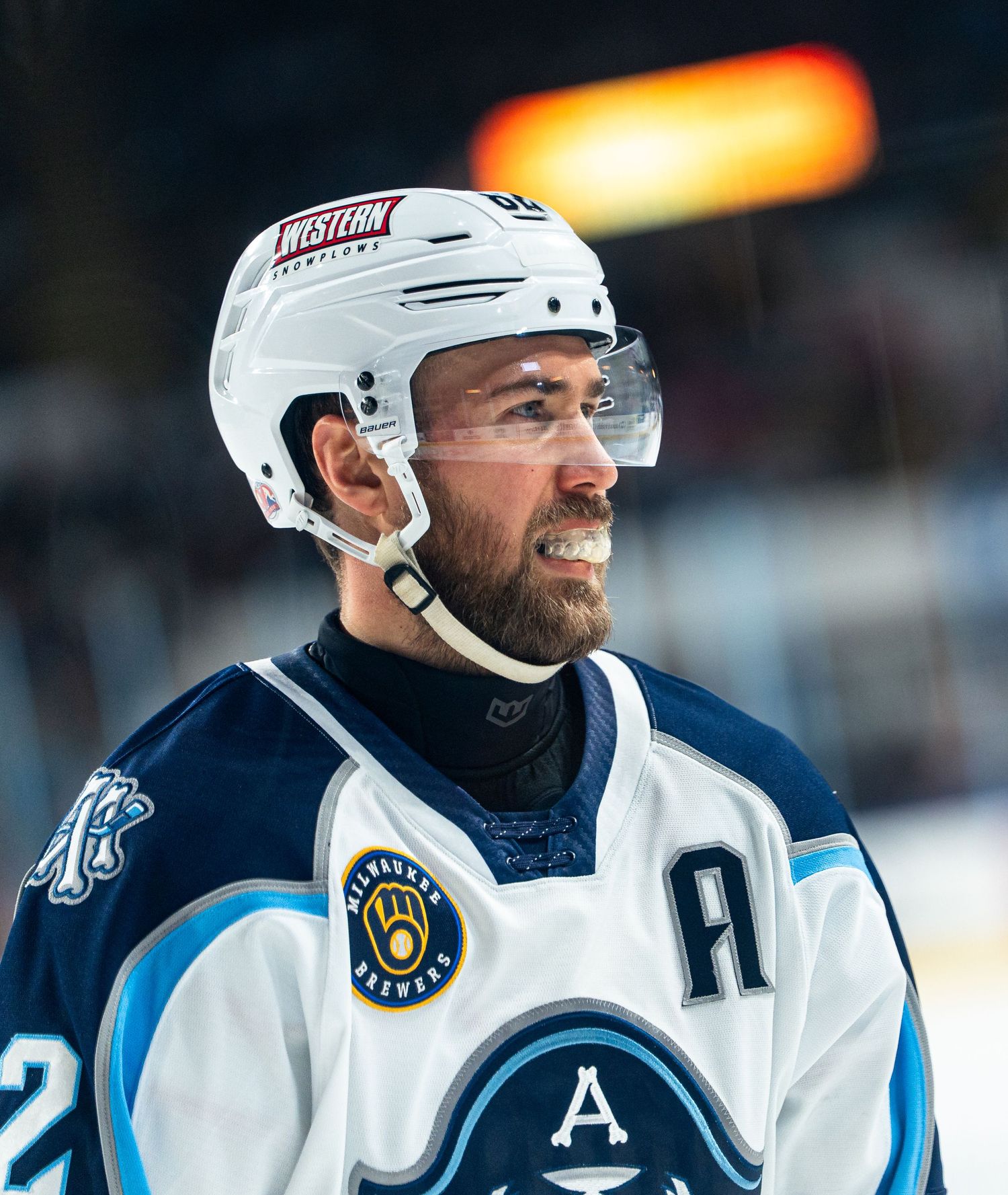 Hockey player wearing white helmet and alternate captain 'A' patch during game.