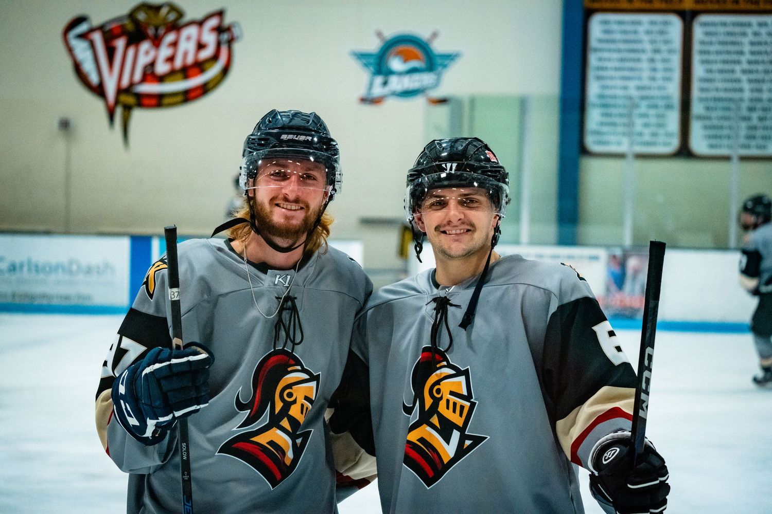 Hockey team members in gray uniforms gather on ice during practice.