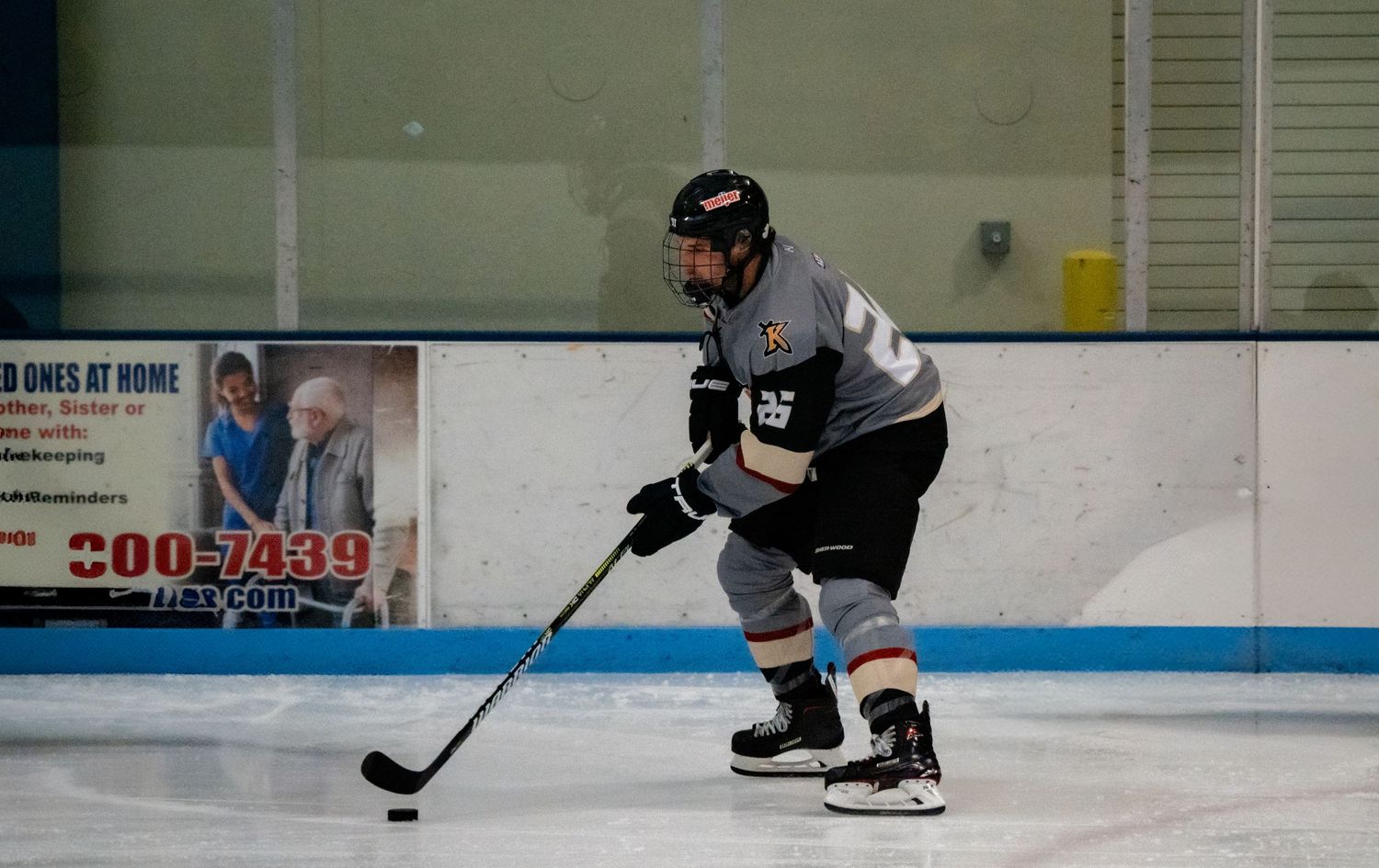 Hockey player in black and gray jersey handles puck on ice rink during practice session.