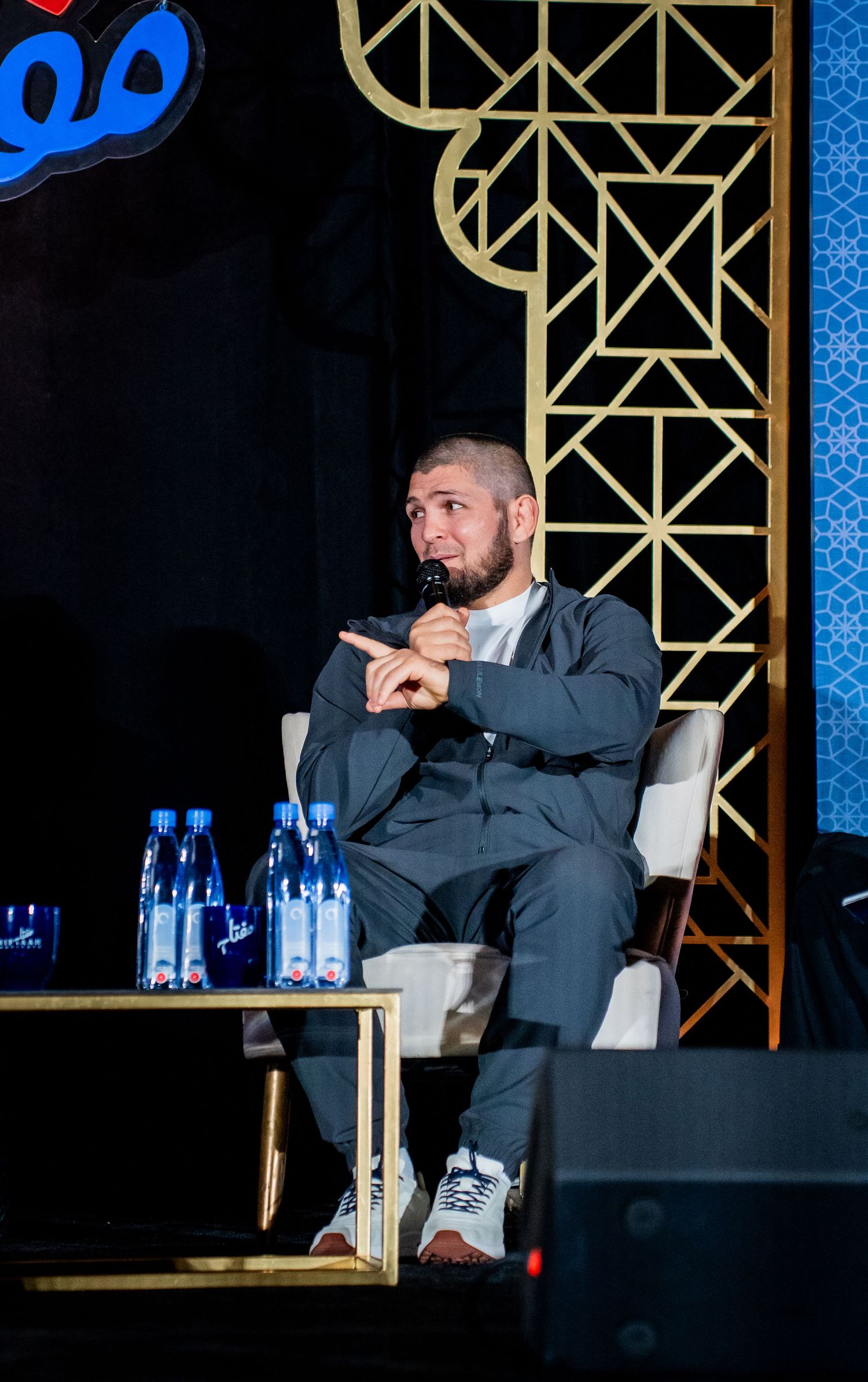 Business panel participants engaged in conversation on stage with branded backdrop.