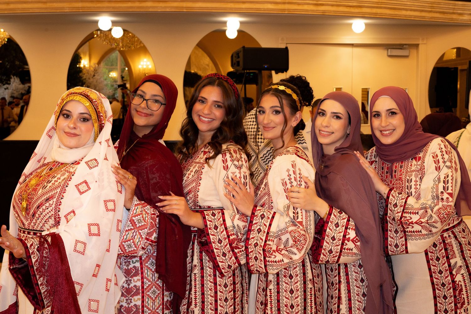 A group wearing coordinated traditional dresses in shades of burgundy and cream pose together at an indoor event.