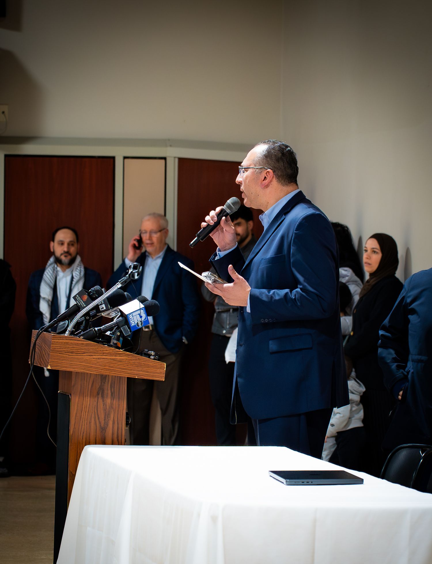 Man in blue suit speaking at podium with microphone at a press conference.