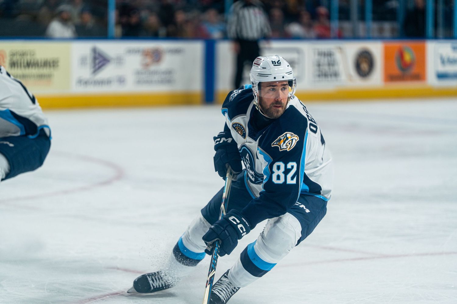 Hockey player number 82 skates in navy and white uniform during game action.