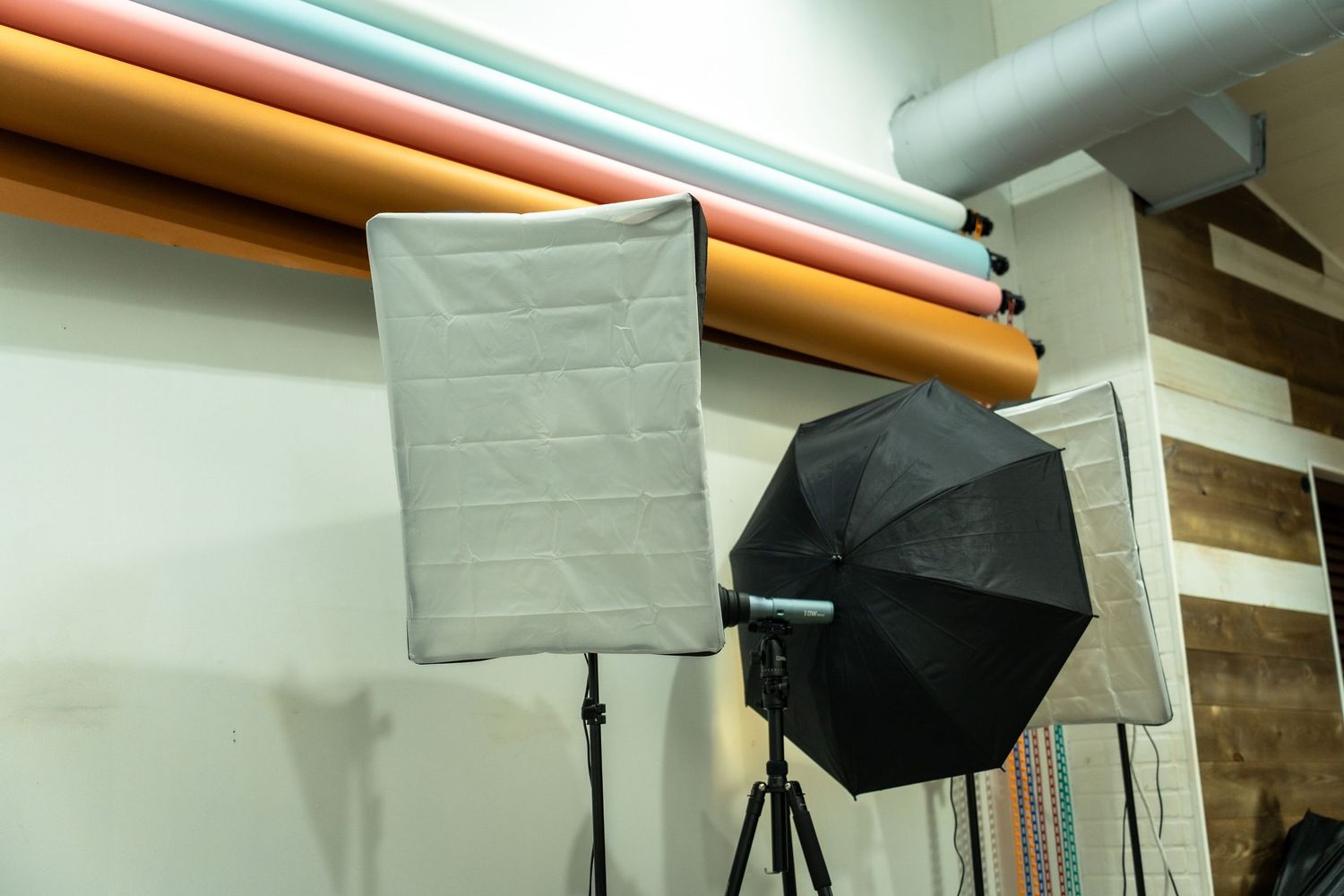 Photography studio setup with lighting equipment including umbrellas, softboxes and reflectors mounted on stands.