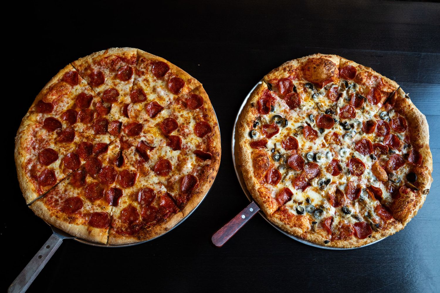 Row of fresh pepperoni pizzas on dark background showing melted cheese and toppings.
