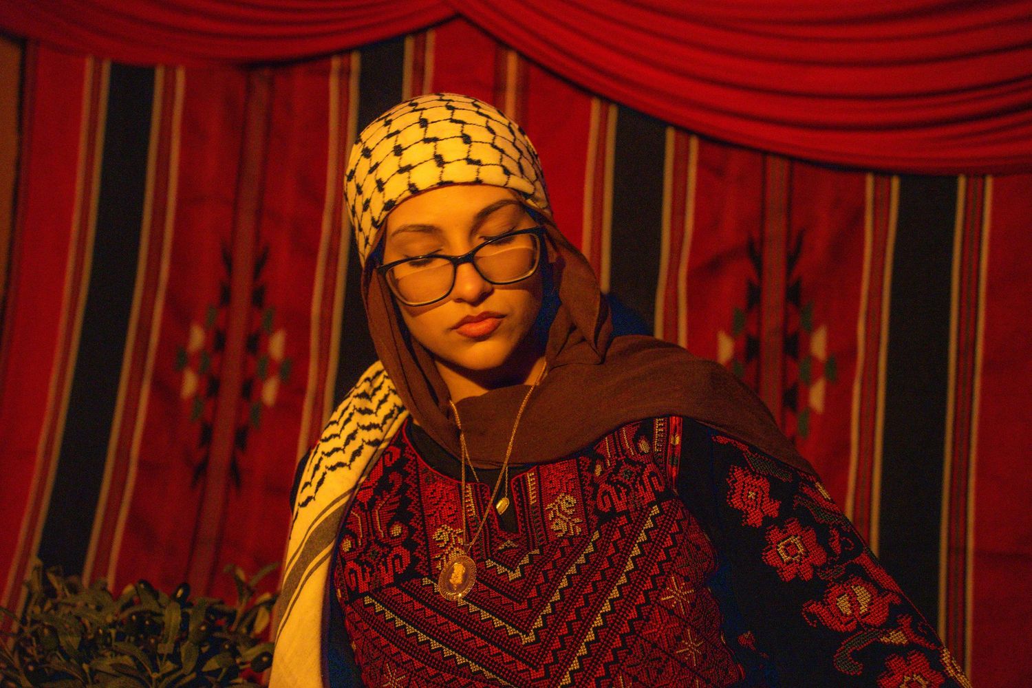 Traditional dress with ornate embroidery and headscarf photographed under dramatic red lighting.