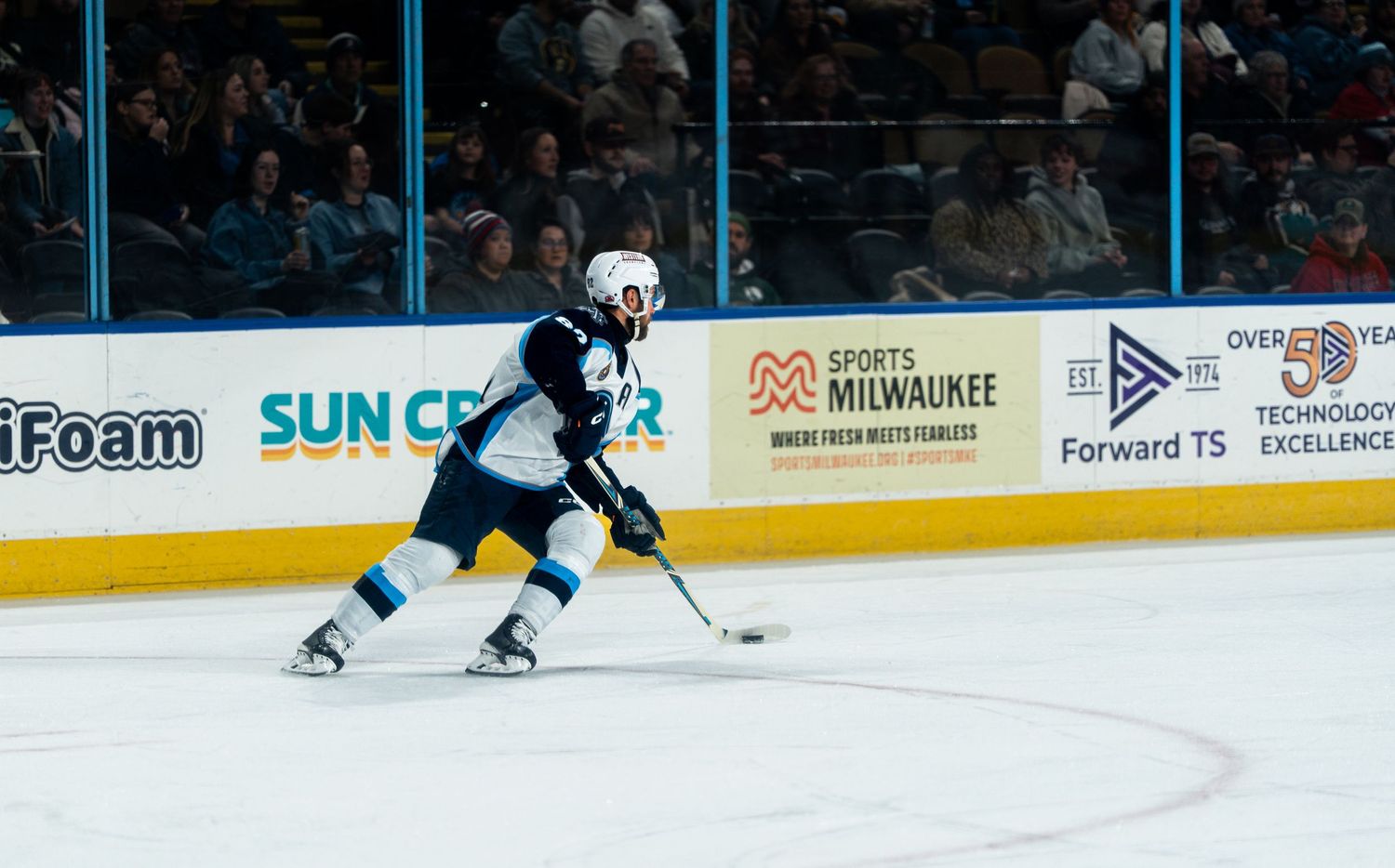 Wide angle view of an ice hockey rink during gameplay showing arena advertising and sponsors.