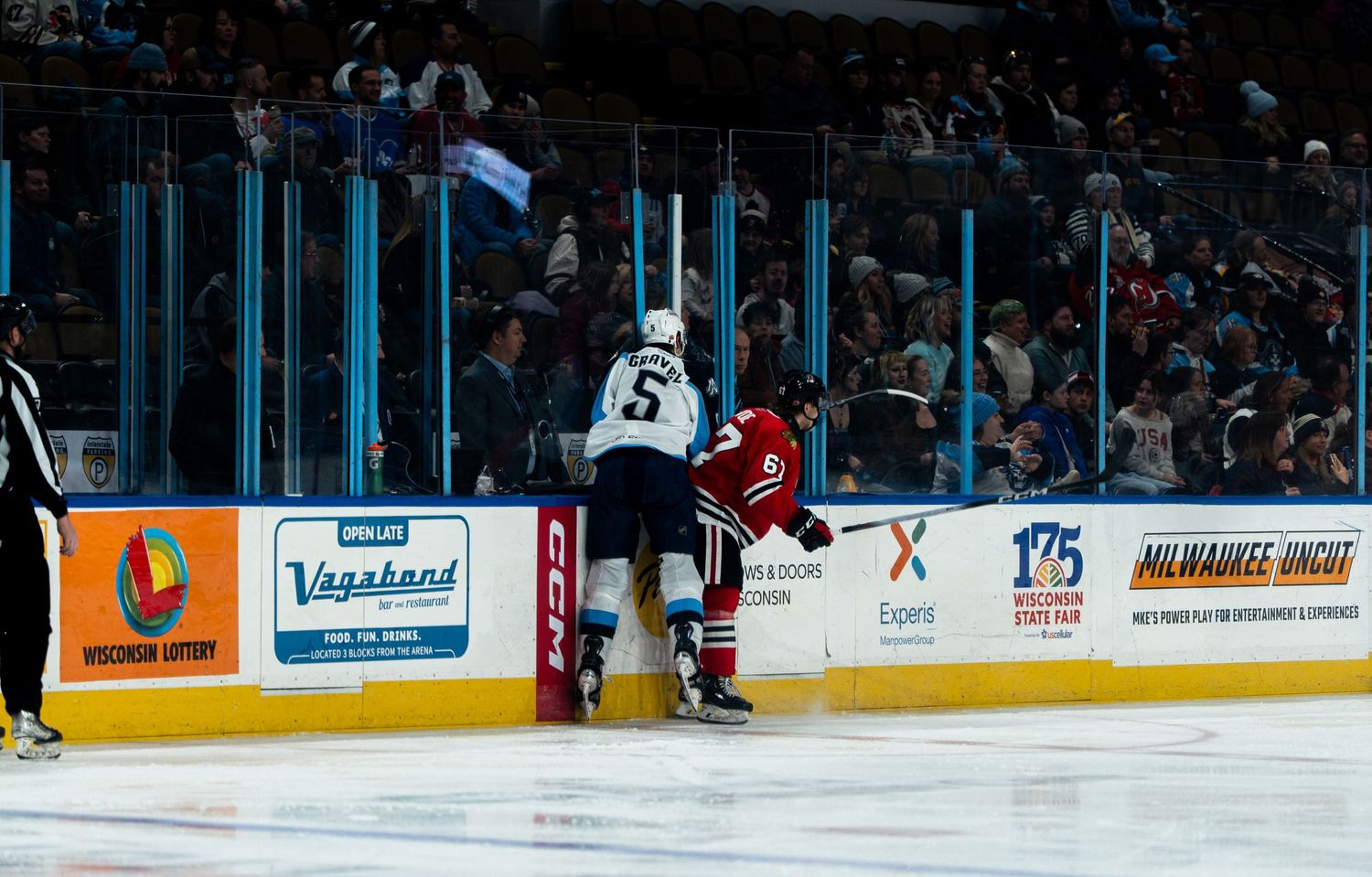 Two hockey players collide against the boards during an intense game with arena advertisements visible in the background.
