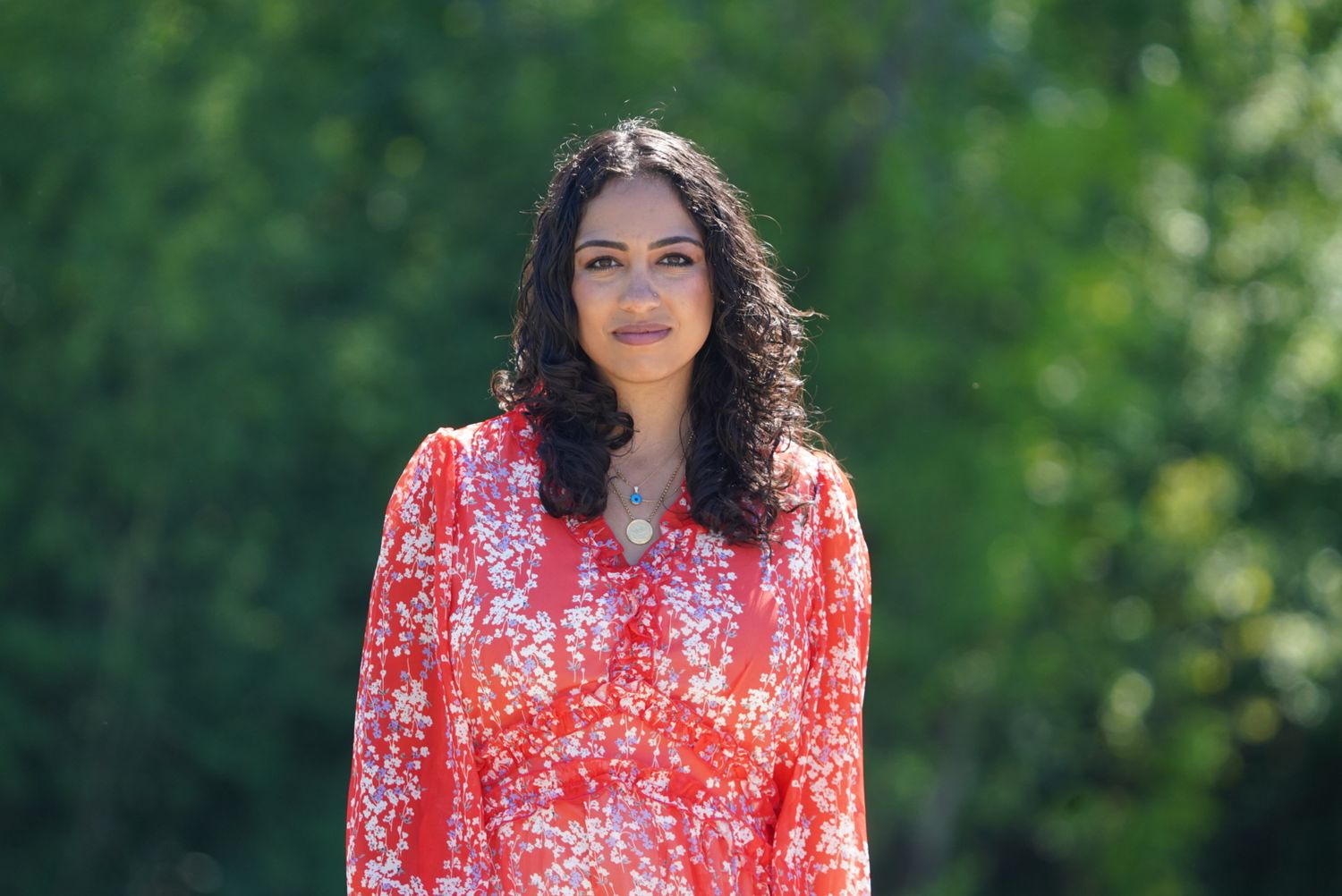 Person wearing vibrant red floral dress poses outdoors in natural setting.