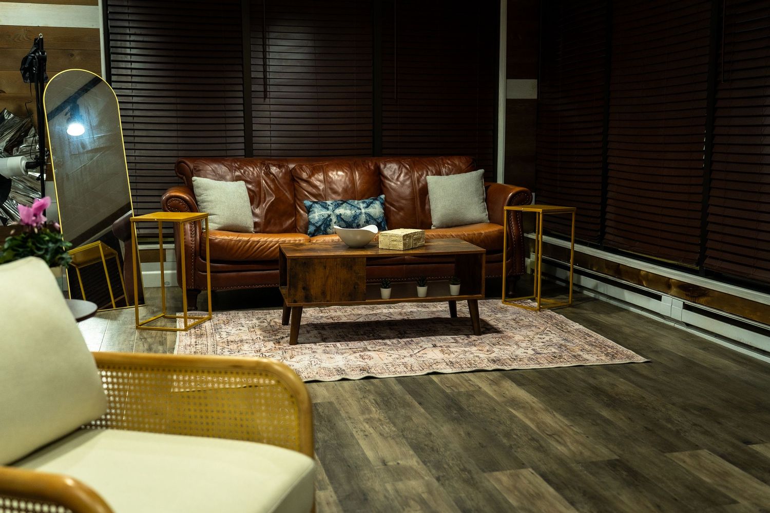 Modern bedroom interior with wooden floors, white bedding, and natural light streaming through horizontal window blinds.