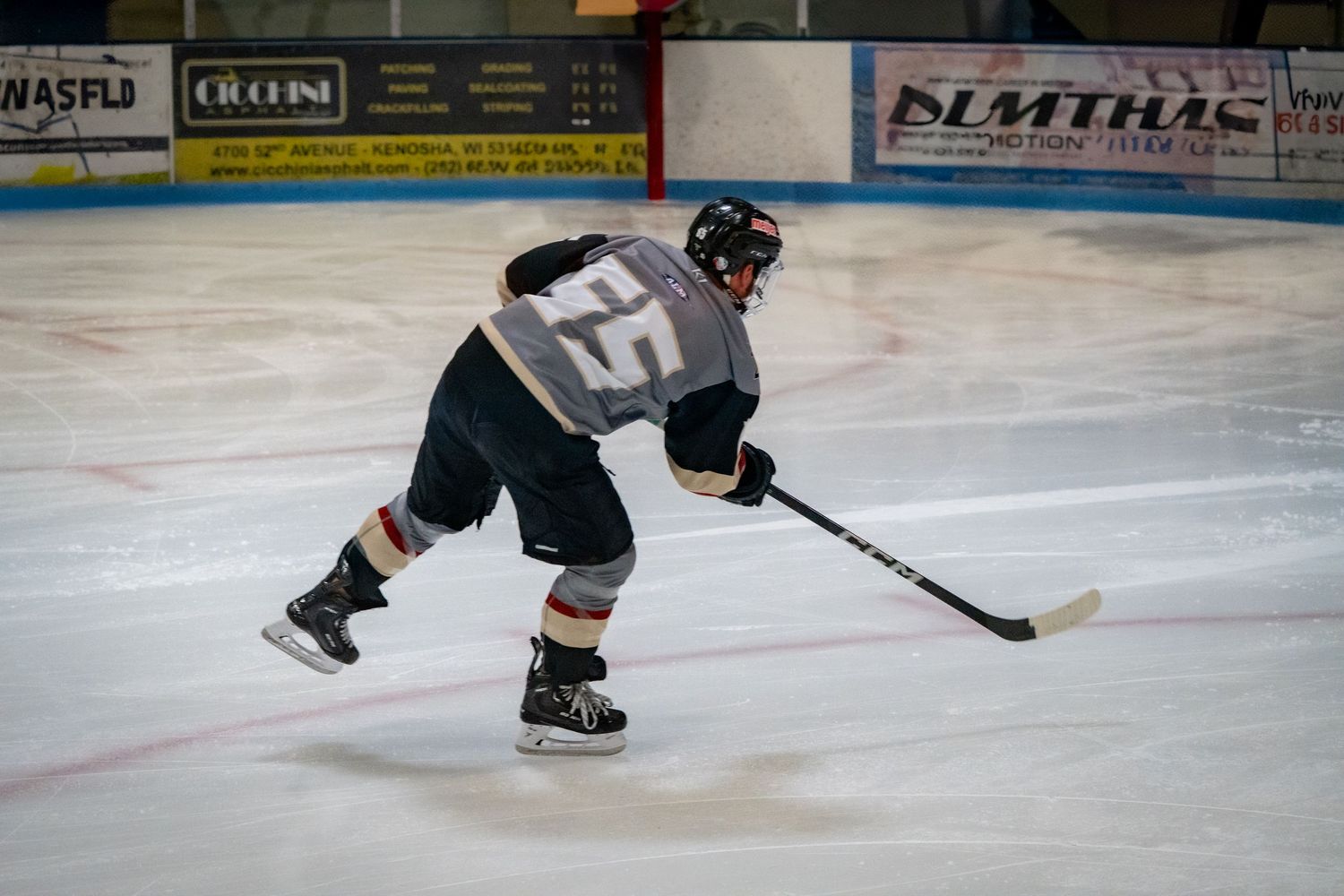 Hockey player in black jersey takes a shot while skating on ice during a game.