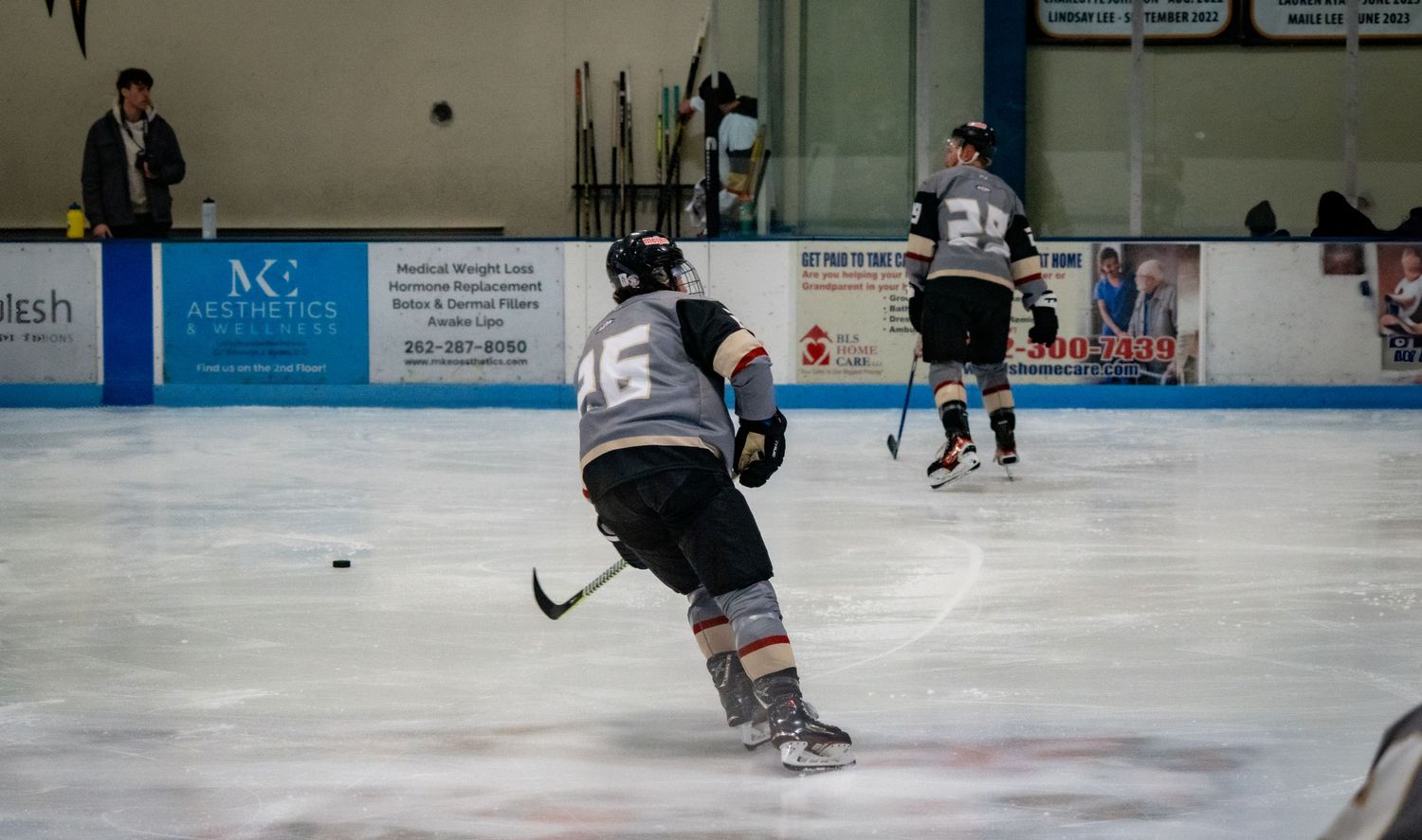Hockey players skate and practice drills on an indoor ice rink during a training session.