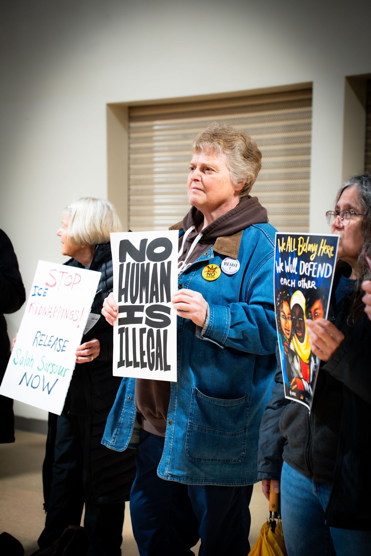 Woman holds No Human Is Illegal protest sign at an immigration rights demonstration indoors.