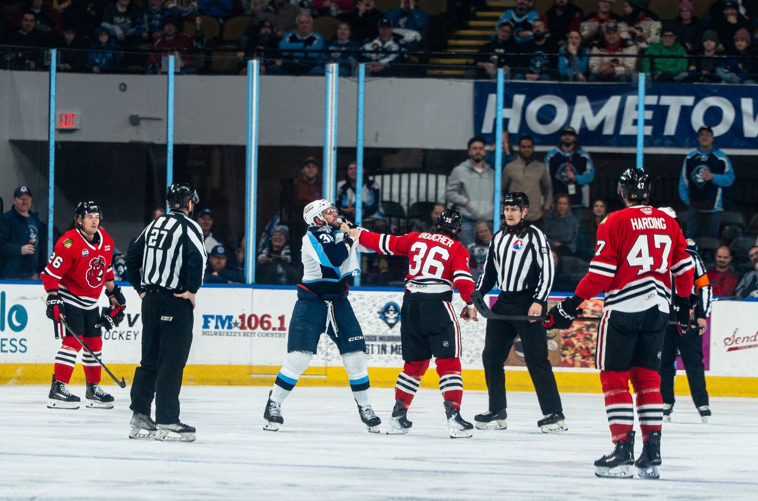 Wide view of hockey players and officials on ice during a game with red jerseys visible.