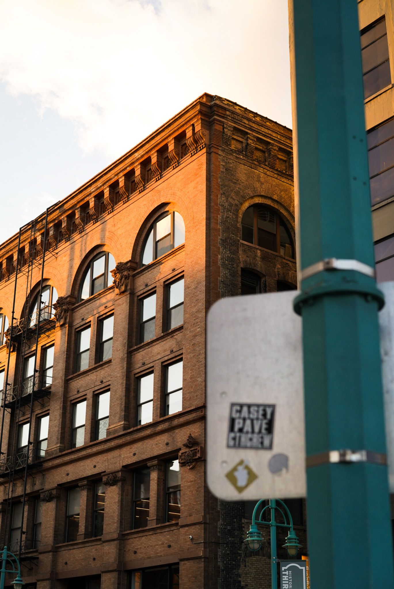 Urban brick building viewed through green metal posts at sunset.