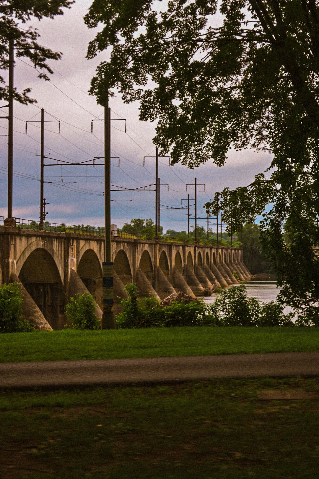 Historic stone bridge with arches and power lines stretching across a river at dusk.