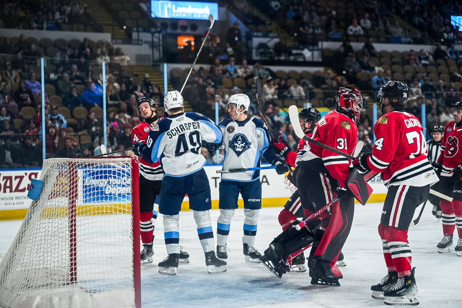 Ice hockey players compete for the puck during an intense professional game with goalies and defenders in position.