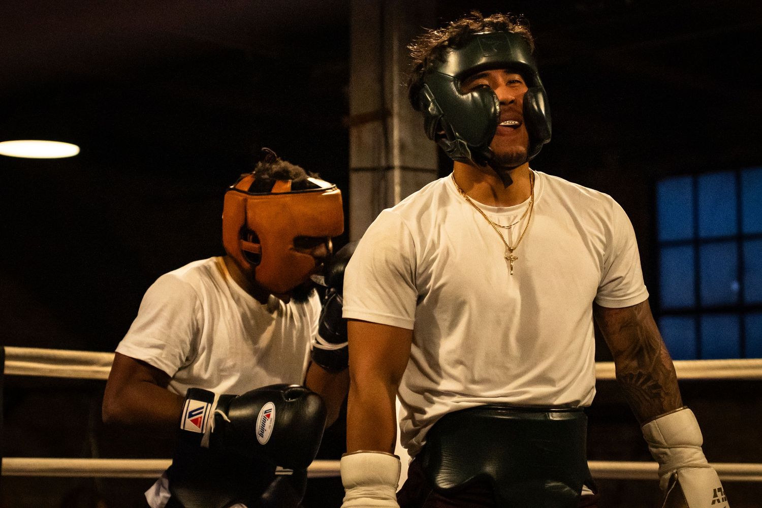 Boxing match underway in atmospheric gym with window light in background.
