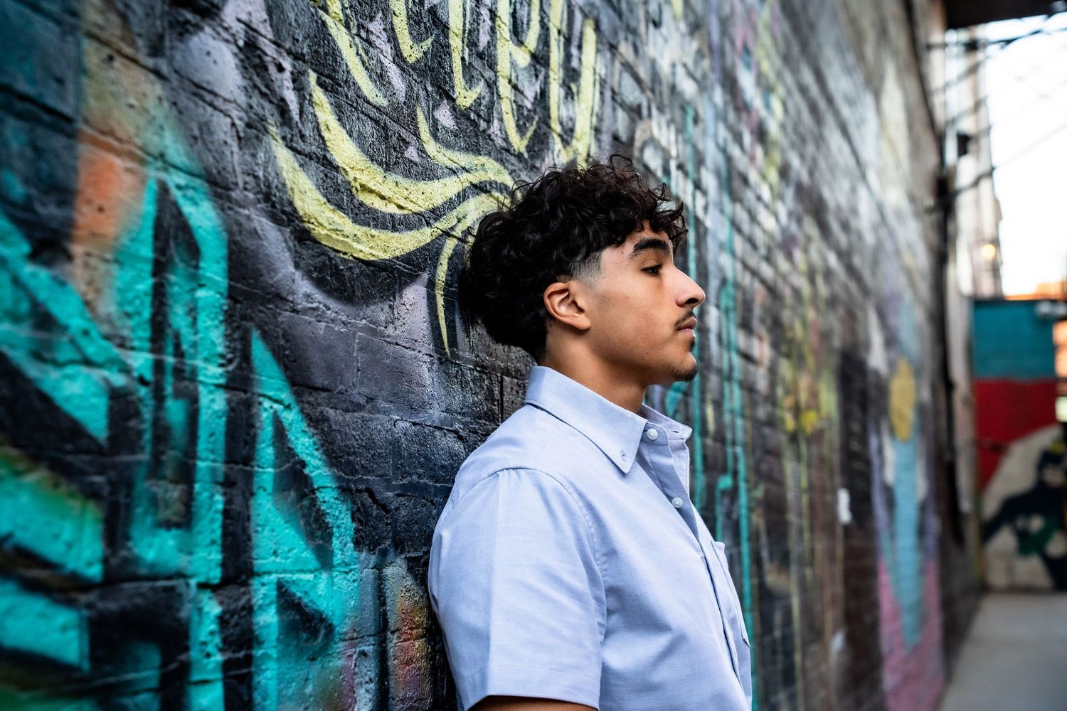 Person in white shirt stands against colorful graffiti wall.