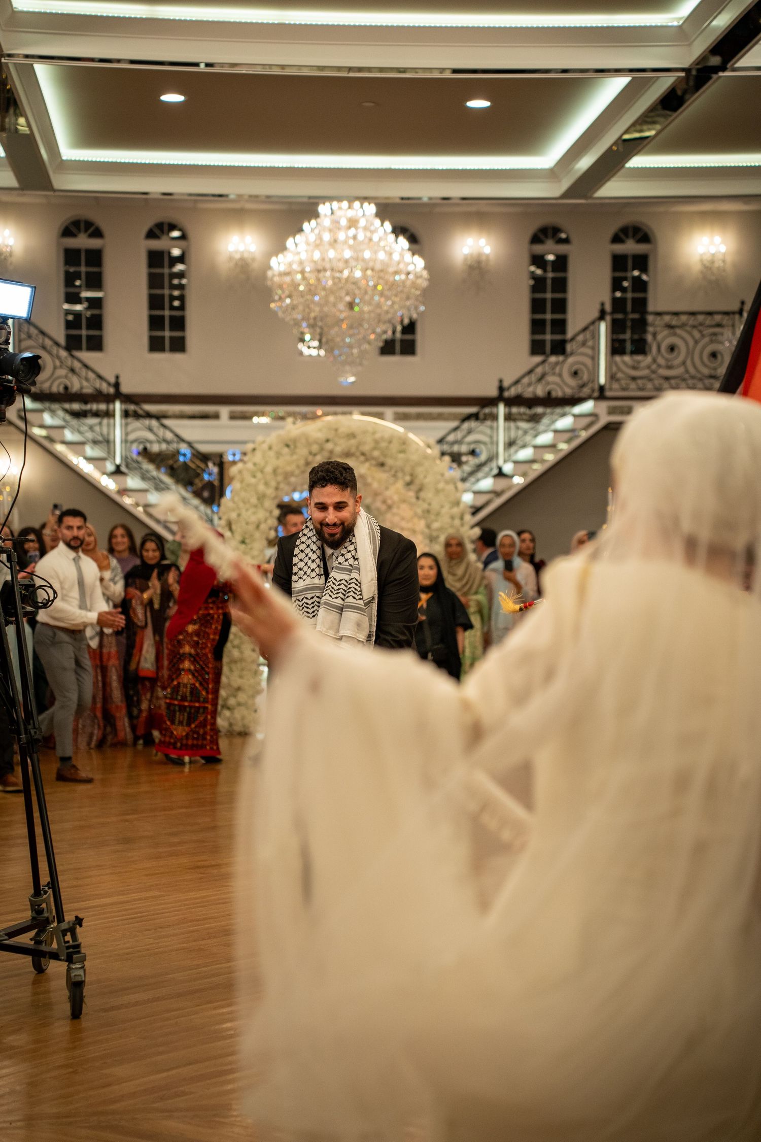 Elegant ballroom with crystal chandelier and grand staircase during a wedding reception.