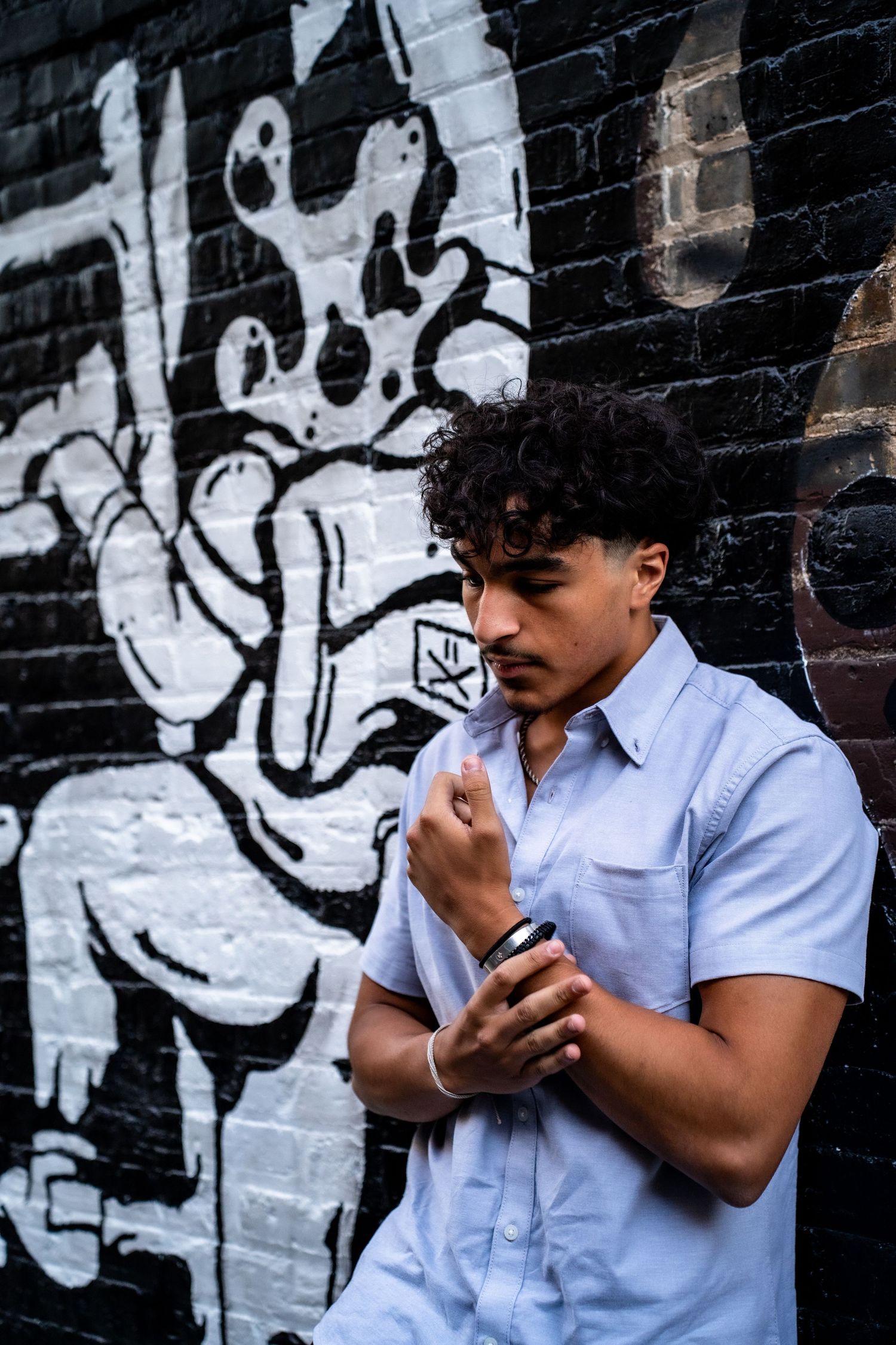 Person in light blue shirt using phone against black and white graffiti wall.