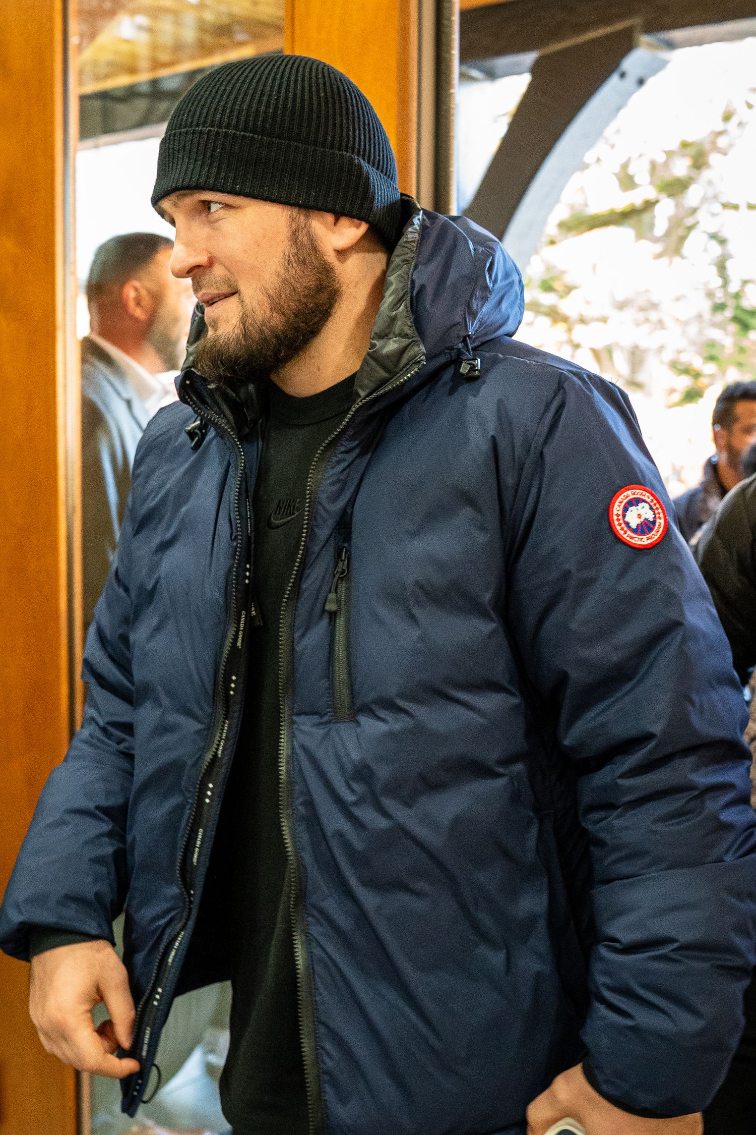 Person wearing a navy Canada Goose parka jacket and black beanie in a warm indoor setting.