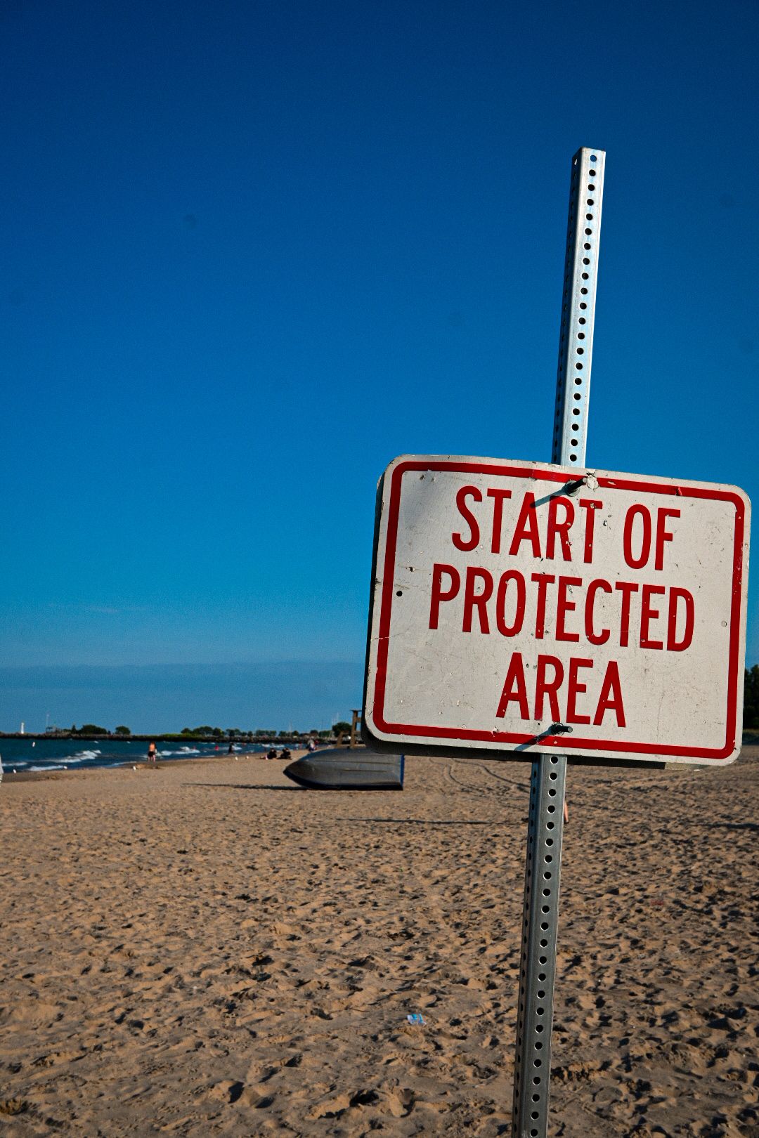 Warning sign marking protected area boundary on sandy beach with clear blue sky.