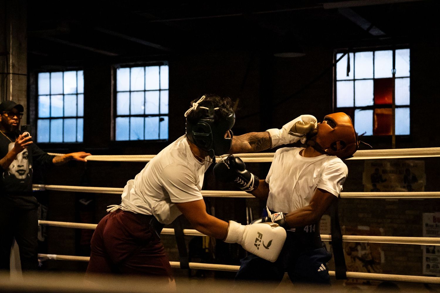Boxing match underway in a traditional gym setting with large windows and ring ropes visible.