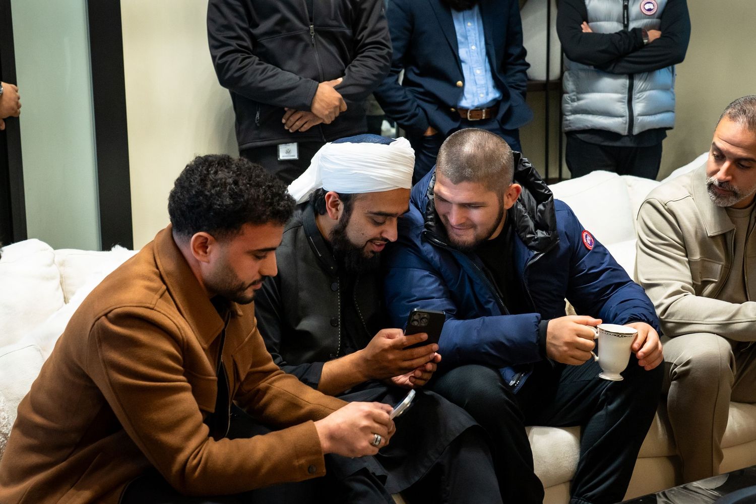 People sitting in a row looking down at their mobile phones while waiting in a public space.