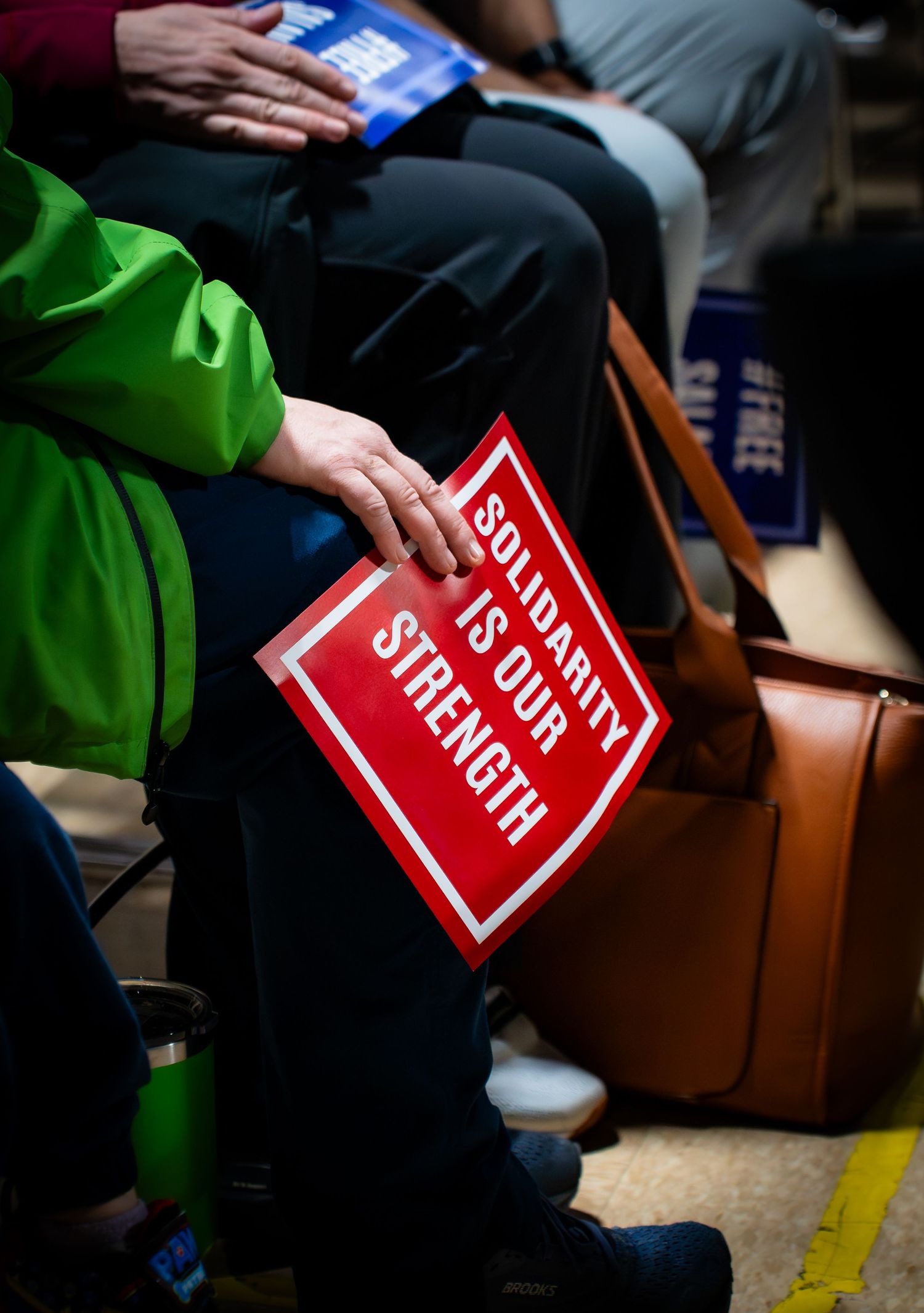 Person in green jacket holds red Solidarity Is Our Strength sign at a political rally or protest event.