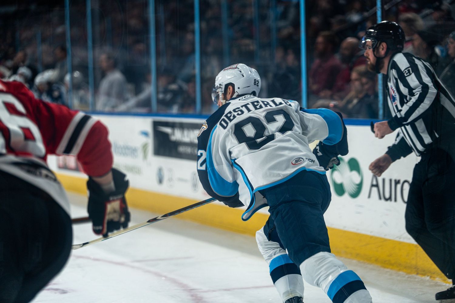 Hockey players chase the puck along the boards during an intense game moment.