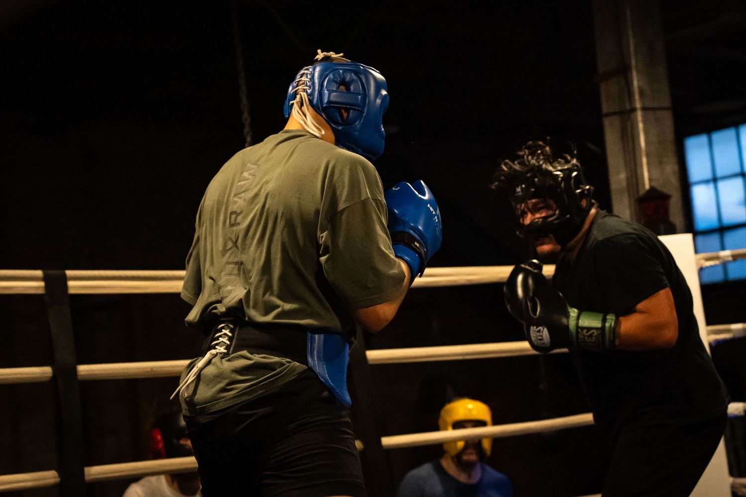 Boxers train in protective gear inside a traditional boxing gym with brick walls.